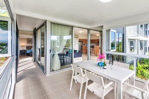 A modern apartment with a balcony, sliding glass doors, a dining area, and a kitchen. - Oasis 1 Hamilton Island 2 Bedroom Apartment In Central Location With Golf Buggy (Whitsundays)