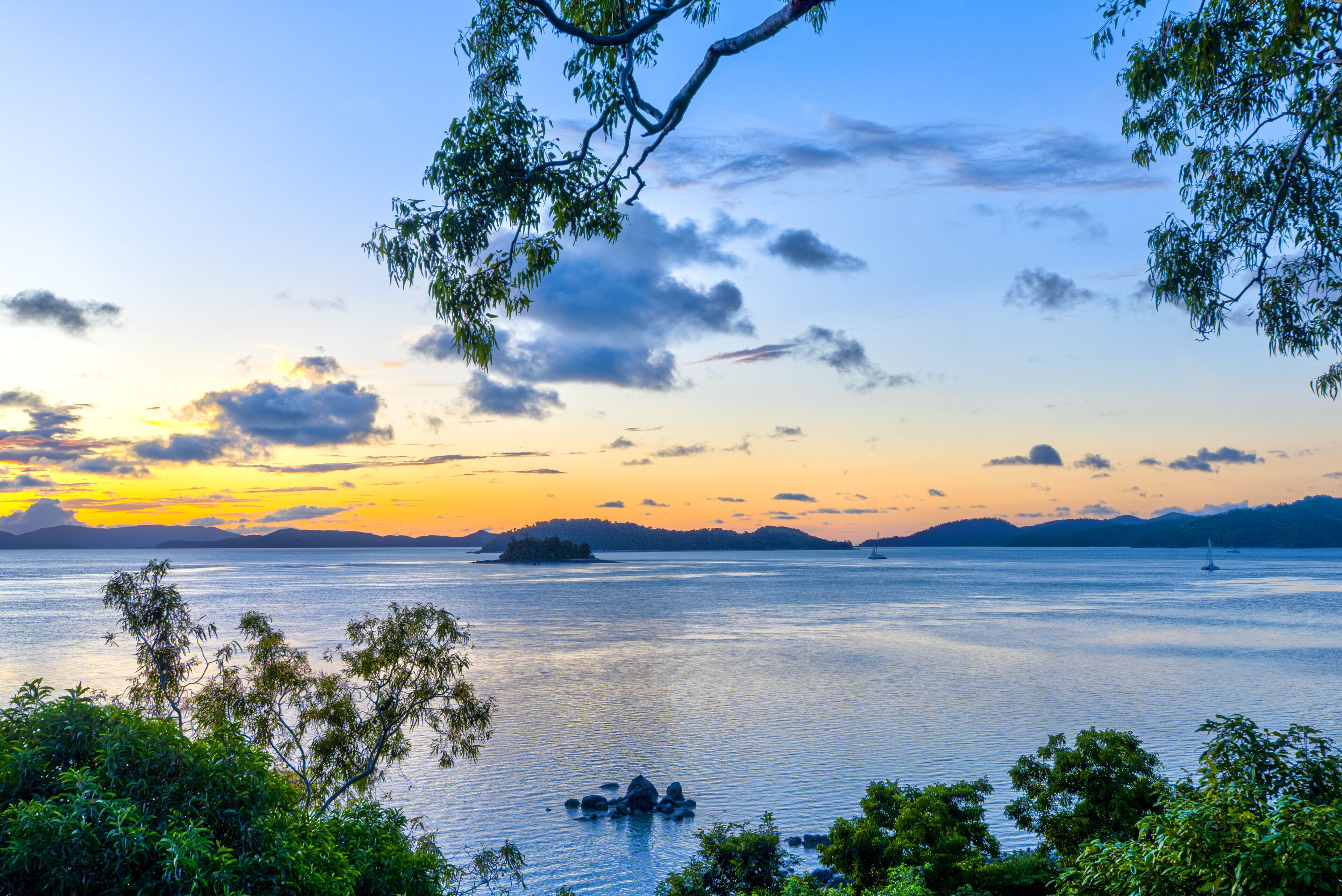 A serene lake at sunset with a distant island and a sailboat.