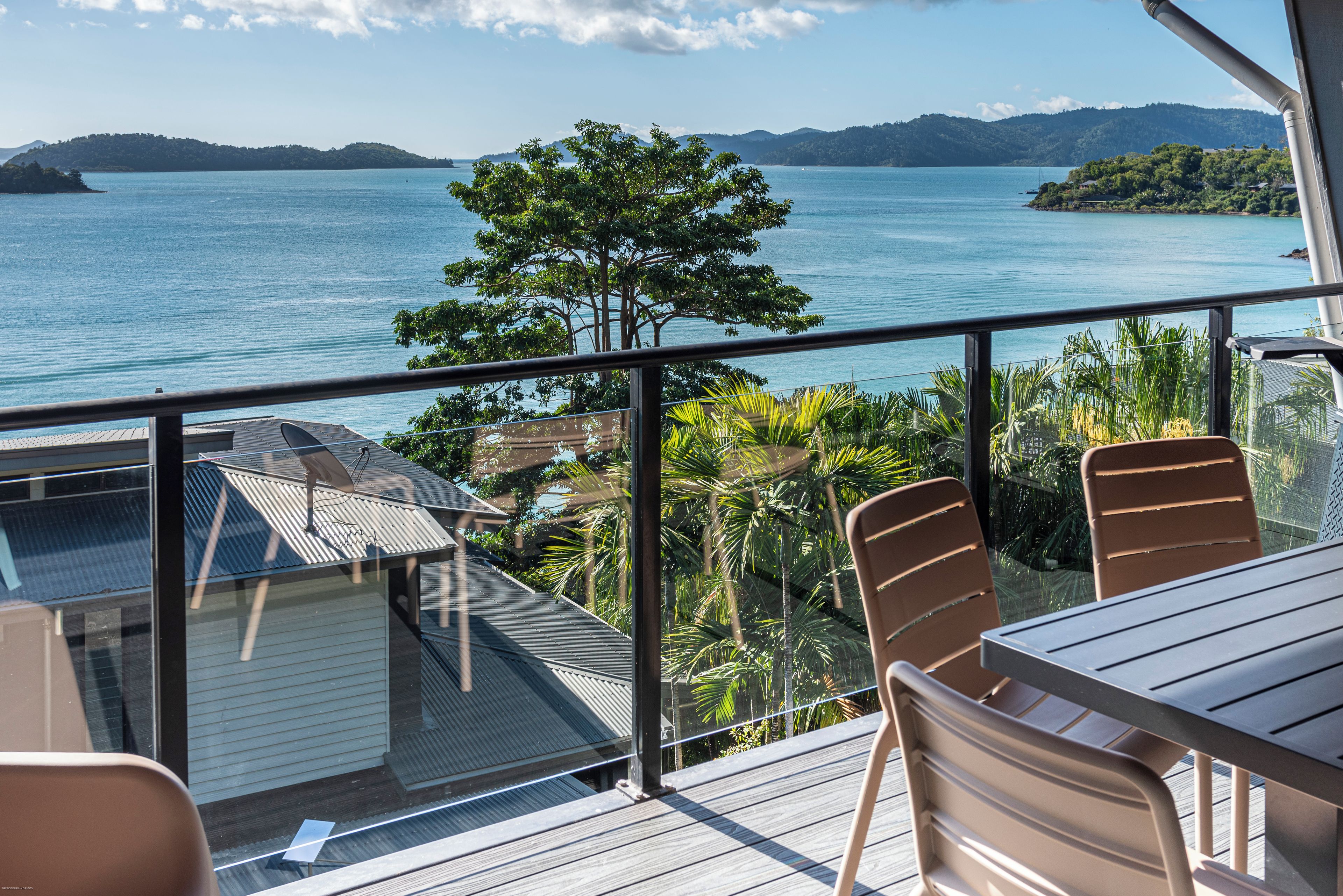 Un balcon donnant sur une vaste étendue d’eau, avec un arbre et une table entourée de chaises.