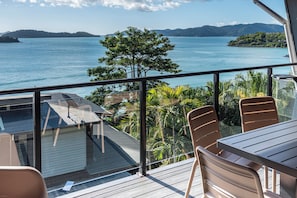 A balcony with a view of a large body of water, a tree, and a table with chairs. - Shorelines 27 Hamilton Island 2 Bedroom Ocean View Near Marina With Golf Buggy (Whitsundays)