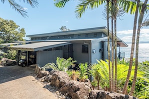 A modern house with a covered porch, a garage, and a view of the sea.