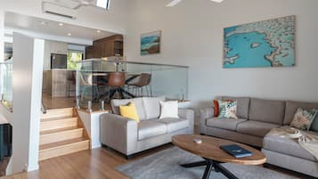 A modern living room with a grey sofa, a coffee table, and a dining area with a glass partition.