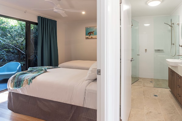 A bedroom with a bed, a bathroom with a shower, and a view of greenery outside.