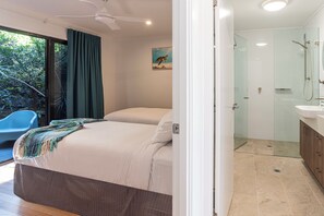 A bedroom with a bed, a bathroom with a shower, and a view of greenery outside. - Shorelines 27 Hamilton Island 2 Bedroom Ocean View Near Marina With Golf Buggy (Whitsundays)