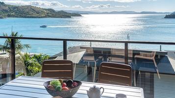 A balcony with a table, chairs, a bowl of fruit, a teapot, and cups.