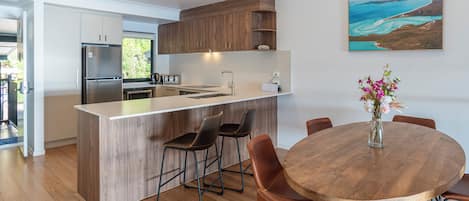 A modern kitchen with a central island, wooden cabinets, and a dining area with a round table and chairs.