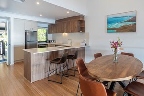 A modern kitchen with a central island, wooden cabinets, and a dining area with a round table and chairs. - Shorelines 27 Hamilton Island 2 Bedroom Ocean View Near Marina With Golf Buggy (Whitsundays)