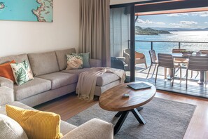 A modern living room with a sofa, coffee table, and a view of the sea through a glass door. - Shorelines 27 Hamilton Island 2 Bedroom Ocean View Near Marina With Golf Buggy (Whitsundays)