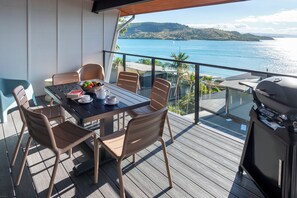 A balcony with a table set for two, chairs, a grill, and a view of the sea. - Shorelines 27 Hamilton Island 2 Bedroom Ocean View Near Marina With Golf Buggy (Whitsundays)