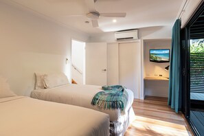 A bedroom with two beds, a ceiling fan, an air conditioning unit, a television, and a view of the outdoors through a sliding door. - Shorelines 27 Hamilton Island 2 Bedroom Ocean View Near Marina With Golf Buggy (Whitsundays)