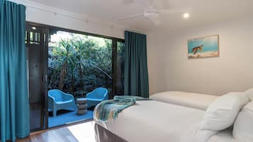 A bedroom with a bed, two chairs, a painting, and a view of greenery through a glass door.