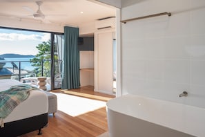 A modern bedroom with a large window, a bed, a bathtub, and a ceiling fan. - Shorelines 27 Hamilton Island 2 Bedroom Ocean View Near Marina With Golf Buggy (Whitsundays)