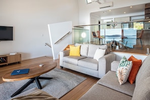 A modern living room with a grey sofa, a coffee table, and a television. - Shorelines 27 Hamilton Island 2 Bedroom Ocean View Near Marina With Golf Buggy (Whitsundays)