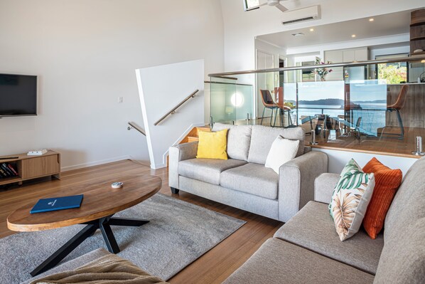 A modern living room with a grey sofa, a coffee table, and a television. - Shorelines 27 Hamilton Island 2 Bedroom Ocean View Near Marina With Golf Buggy (Whitsundays)