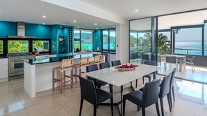 A modern kitchen with a large island, dining area with chairs, and a view of the sea. - Villa 12 The Edge Oceanfront Deluxe 3 Bedroom Near Marina With Golf Buggy (Whitsundays)