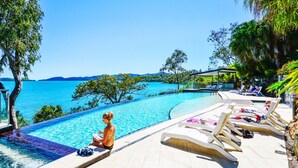 A poolside area with lounge chairs and a view of the sea. - Villa 12 The Edge Oceanfront Deluxe 3 Bedroom Near Marina With Golf Buggy (Whitsundays)