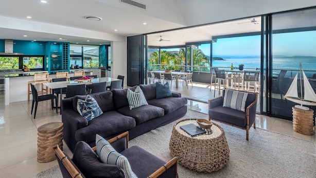 A modern living room with a large sofa, armchairs, and a dining area with a view of the ocean. - Villa 12 The Edge Oceanfront Deluxe 3 Bedroom Near Marina With Golf Buggy (Whitsundays)