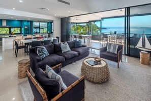 A modern living room with a large sofa, armchairs, and a dining area with a view of the ocean. - Villa 12 The Edge Oceanfront Deluxe 3 Bedroom Near Marina With Golf Buggy (Whitsundays)