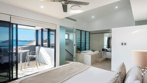 A modern bedroom with a large bed, a balcony with a view, a bathroom with a bathtub, and a desk with a chair. - Villa 12 The Edge Oceanfront Deluxe 3 Bedroom Near Marina With Golf Buggy (Whitsundays)