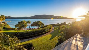 A landscaped garden with a pathway, palm trees, and a view of a lake and distant hills.