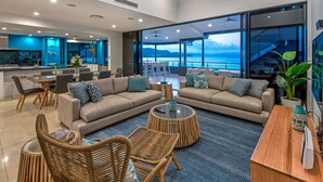 A modern living room with sofas, chairs, and a dining area. It features large windows with a view of the sea. - Villa 16 The Edge Oceanfront Deluxe 3 Bedroom Near Marina With Golf Buggy (Whitsundays)