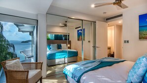 A modern bedroom with a large bed, a glass door leading to a balcony, and a view of the sea. - Villa 16 The Edge Oceanfront Deluxe 3 Bedroom Near Marina With Golf Buggy (Whitsundays)