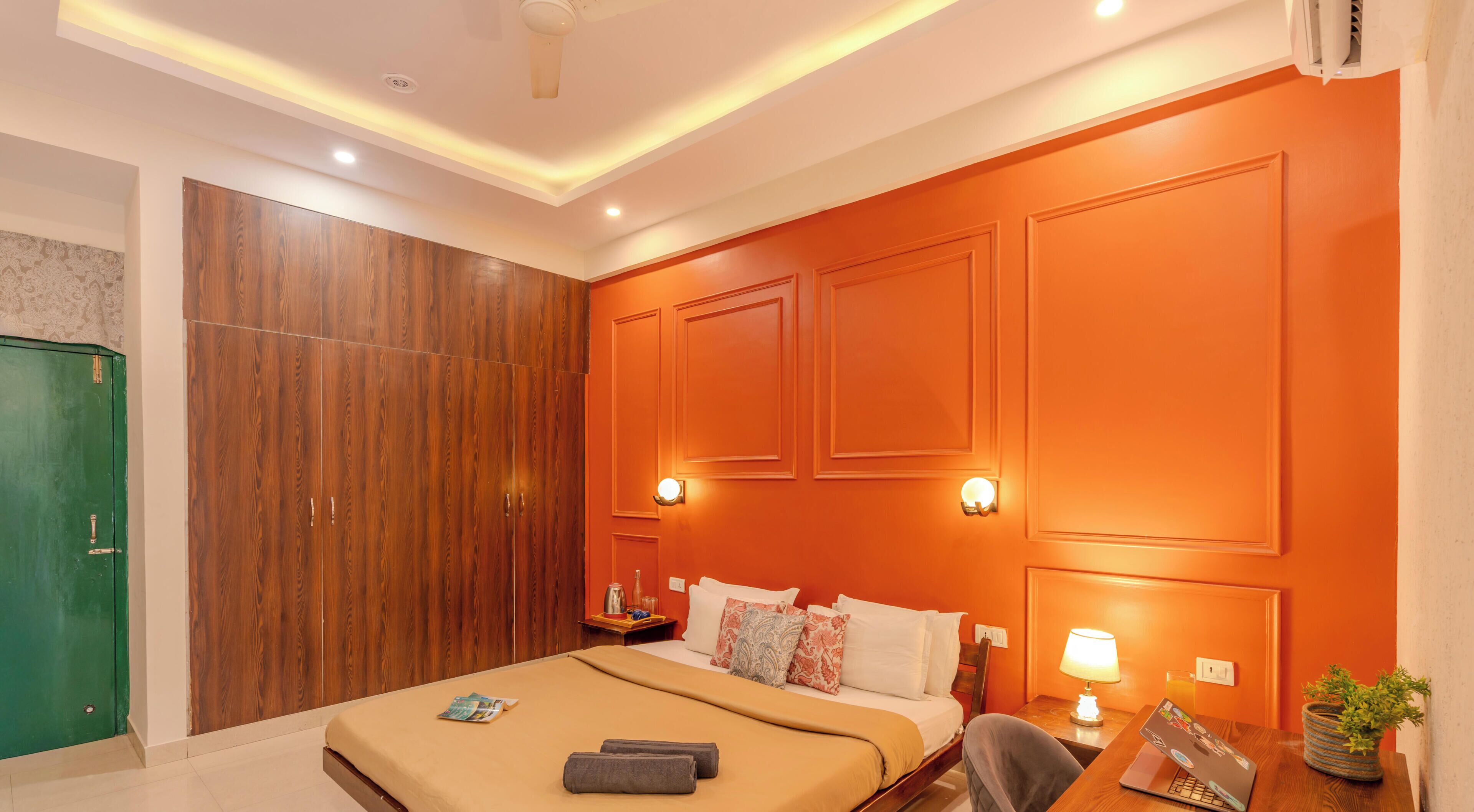 A hotel room with a bed, bedside tables, a green wardrobe, and a wall with built-in lighting.