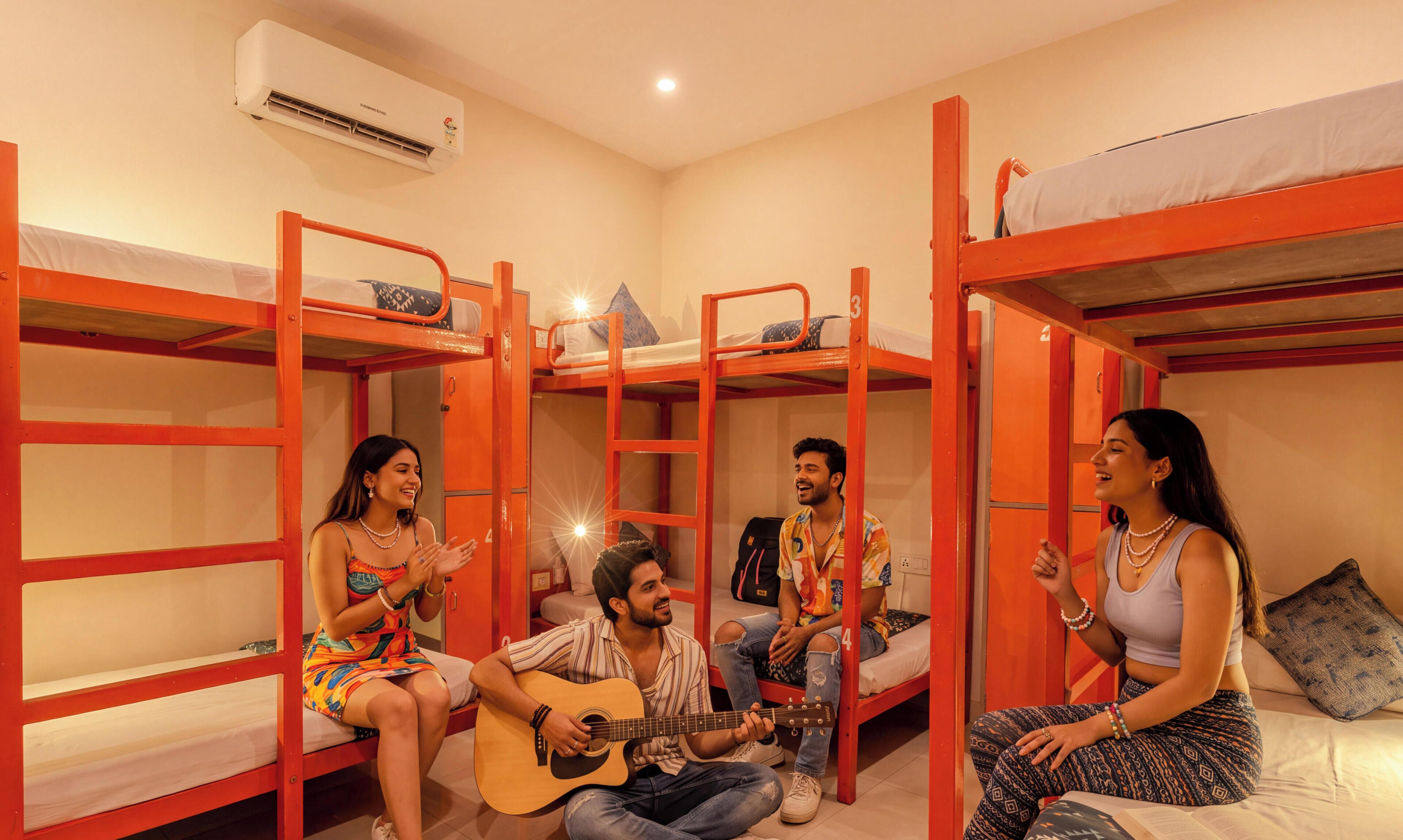 Une chambre de dortoir avec des lits superposés, une guitare et une personne qui en joue.