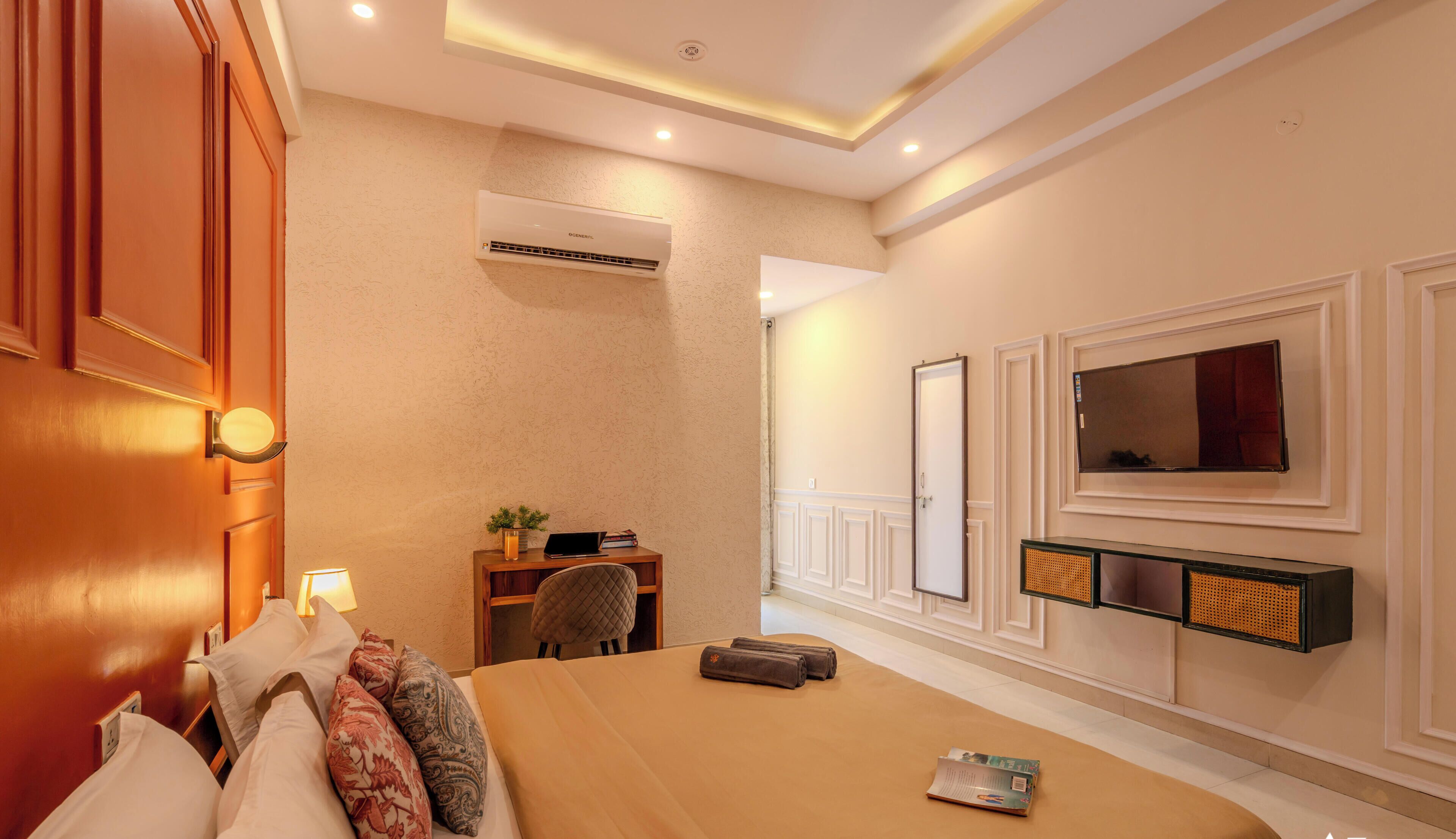 Habitación de hotel con cama, mesita de noche, lámpara, aire acondicionado, televisión y espejo.