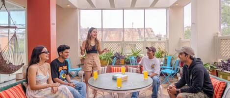 Un groupe de personnes est assis autour d’une table ronde dans un espace ouvert et bien éclairé, avec vue sur l’extérieur.