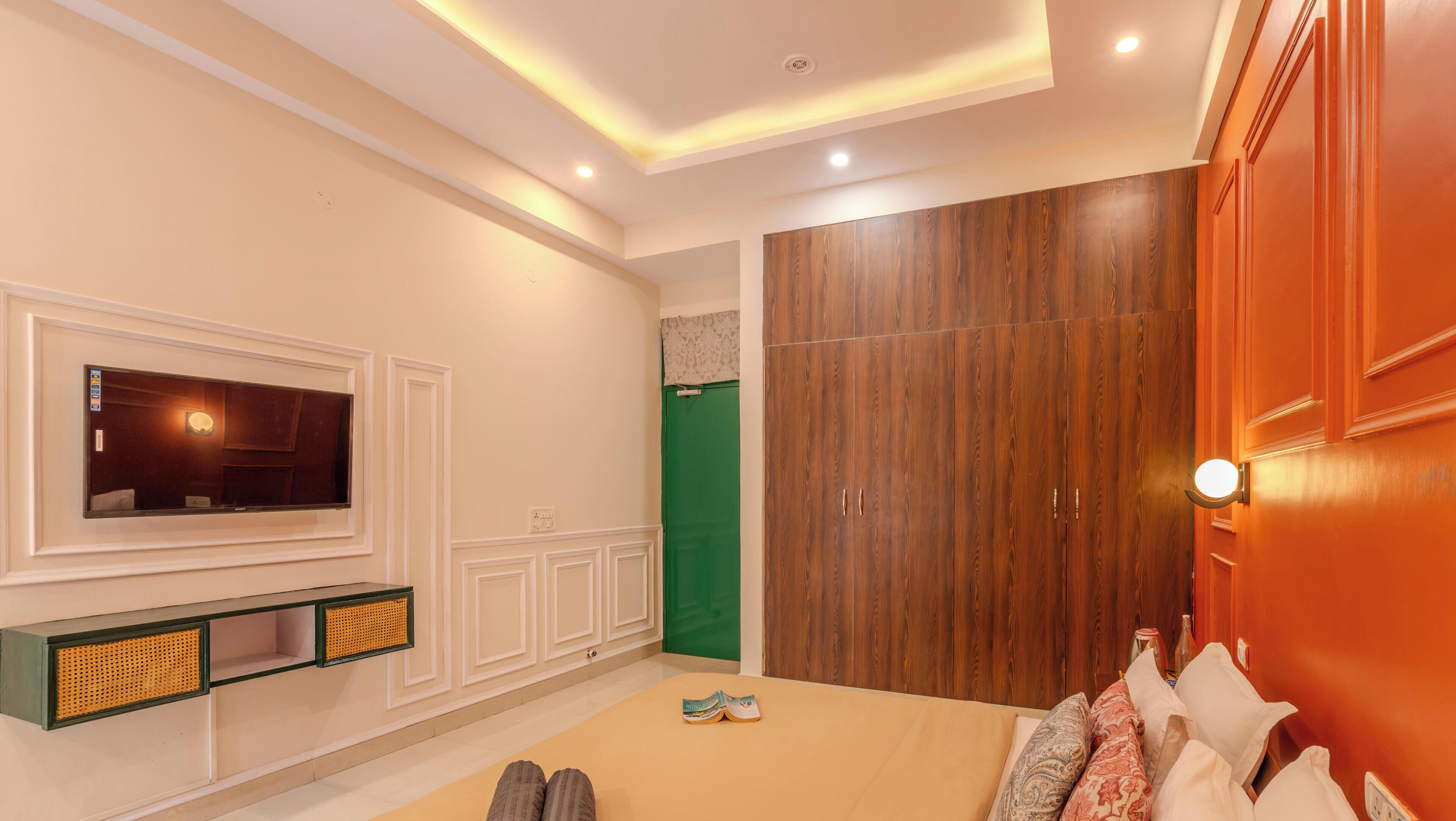 Une chambre à coucher avec un lit, un téléviseur fixé au mur, une armoire et une porte verte.