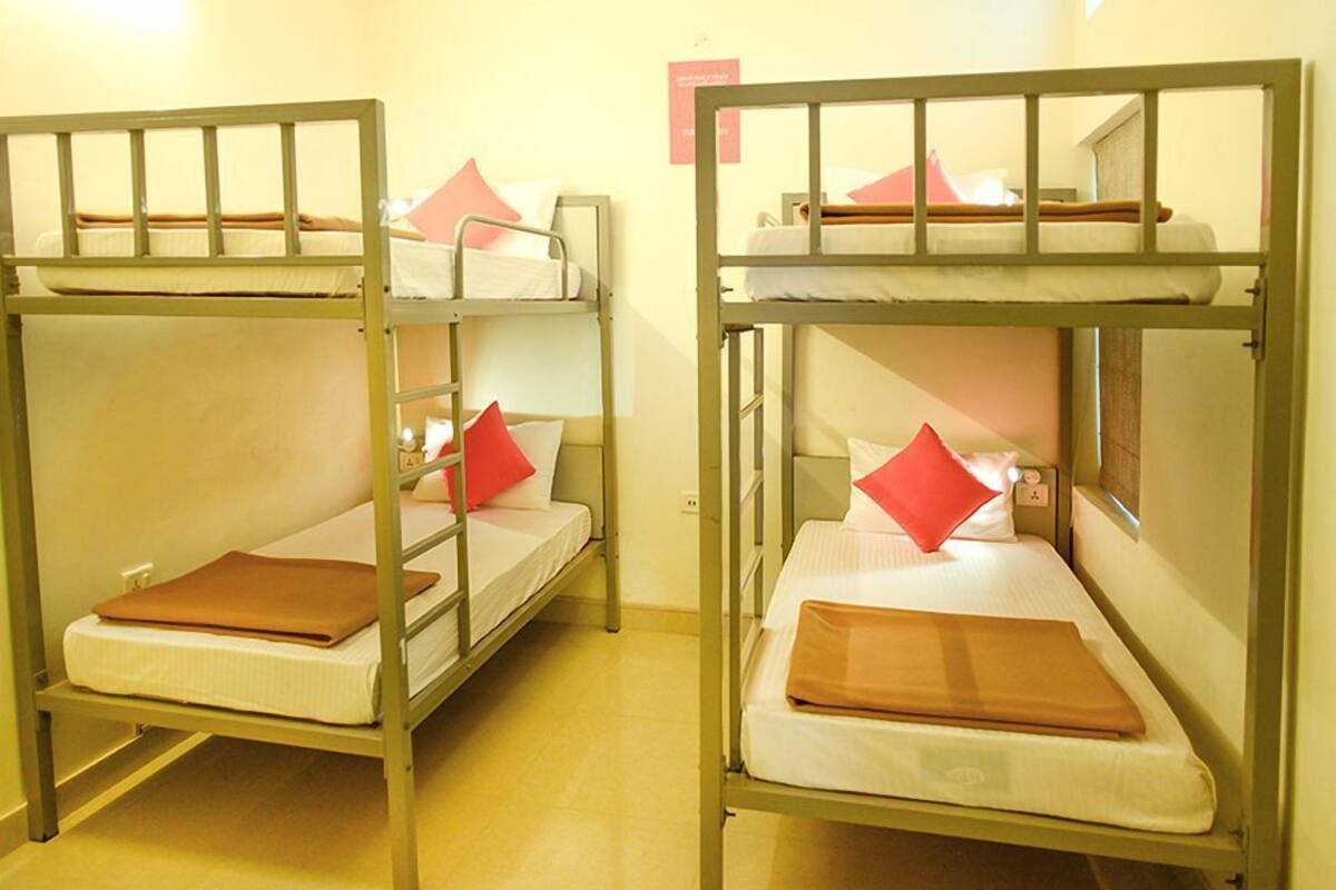 Dos literas con almohadas y una manta, en una habitación con piso y paredes de color claro.