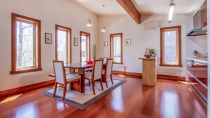 A spacious dining area with a wooden table and chairs, large windows, and a kitchen area with modern appliances. - Cocoa Niseko (Kutchan)