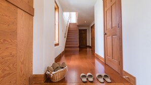 A wooden interior hallway with a staircase, wooden doors, and a basket with slippers. - Cocoa Niseko (Kutchan)