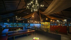 An indoor space with a high ceiling, hanging lights, and a seating area with tables and benches. - Zostel Kochi (Fort Kochi) (Kochi)