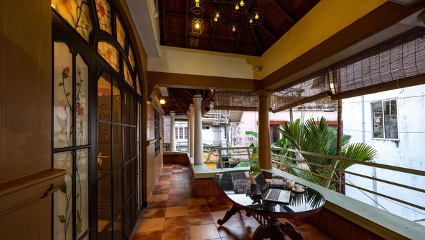 A corridor with a checkered floor, a glass table with a laptop, and a view of the outside through large windows. - Zostel Kochi (Fort Kochi) (Kochi)