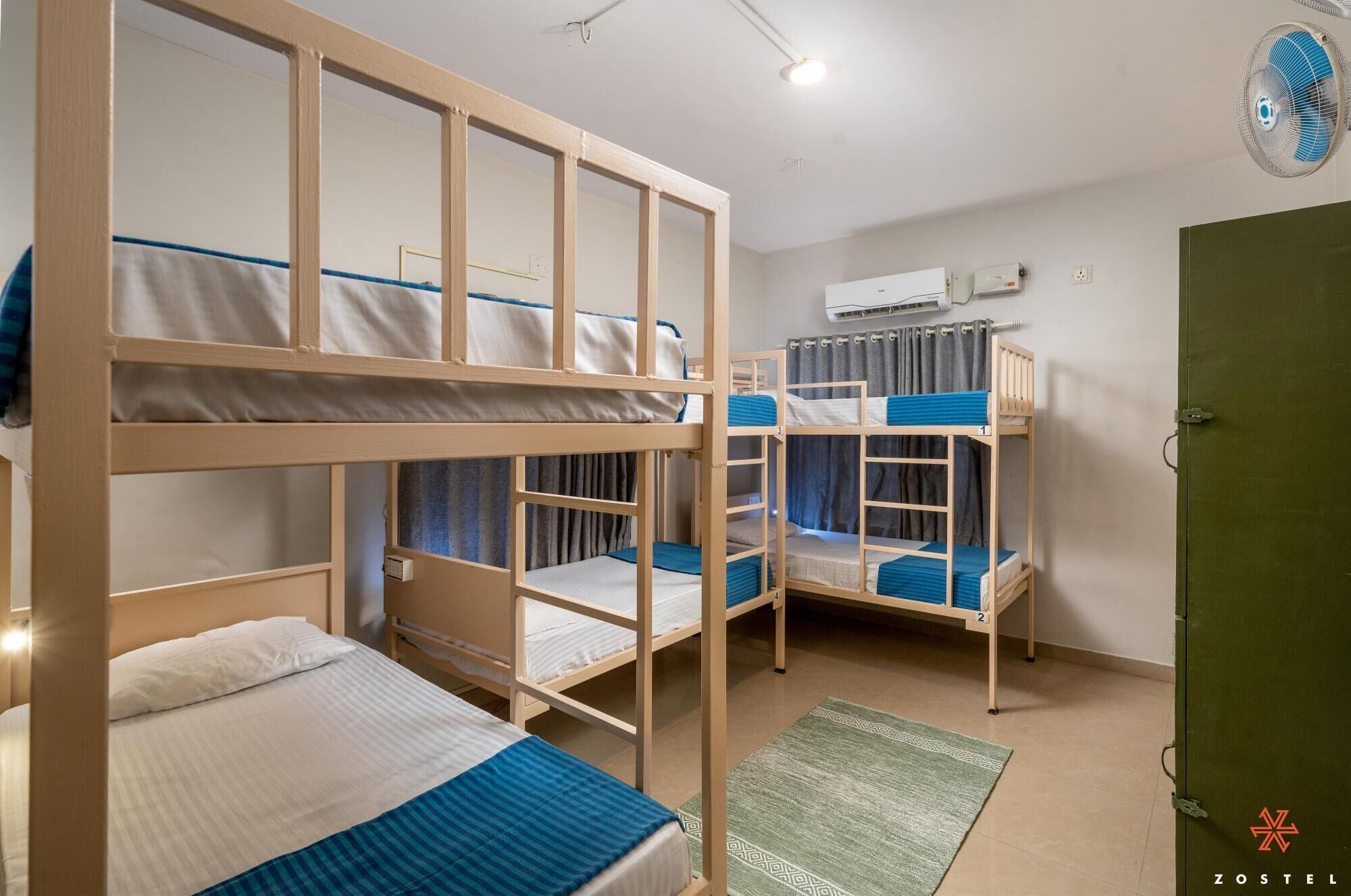 Une chambre de dortoir avec des lits superposés, un tapis vert, un appareil de climatisation et une porte.