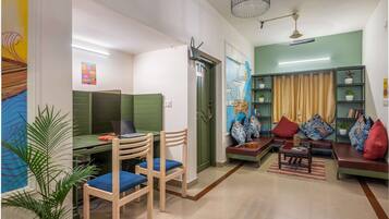 A modern living room with a green sofa, a dining area with a table and chairs, and a bookshelf with decorative items.