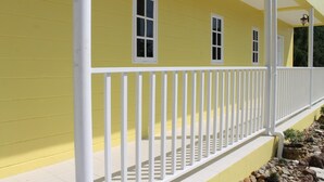 A yellow building with a white porch and railing, featuring three windows and a small sign.