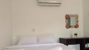 A hotel room with a bed, white linens, a decorative mirror, and a small desk with a plant.