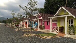 A row of colorful cabins with a gravel driveway and a mountainous backdrop.