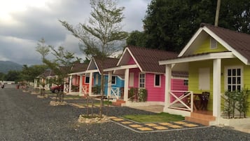 A row of colorful cabins with a gravel driveway and a mountainous backdrop.