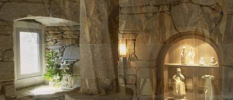 Interior de paredes de pedra, com uma pequena janela e uma vitrine com estátuas.