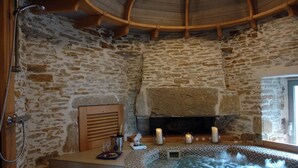 A stone-walled spa room with a hot tub, candles, and a fireplace. - La Vinotière (Le Conquet)