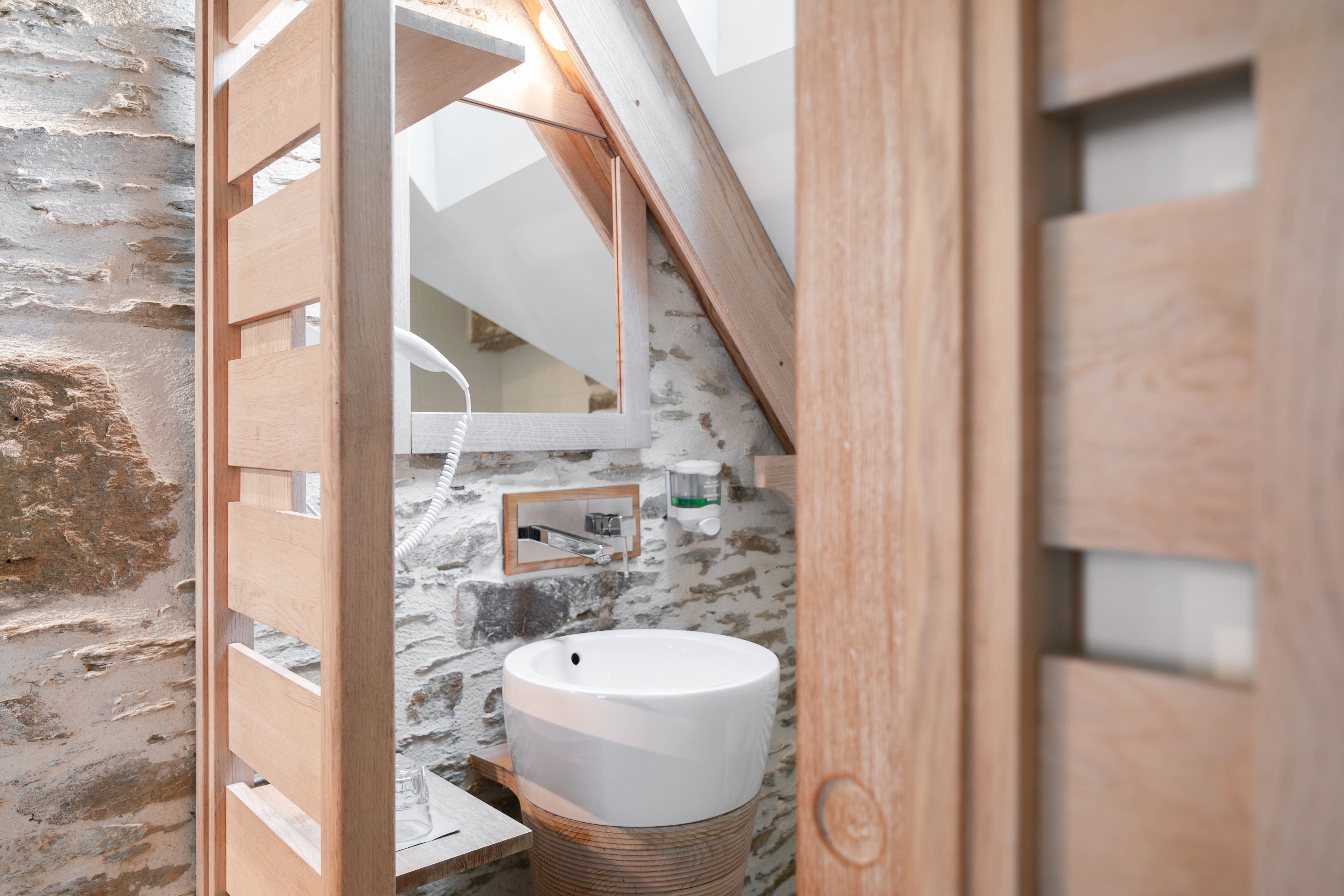 A rustic bathroom with a stone wall, wooden door, and a large white basin.