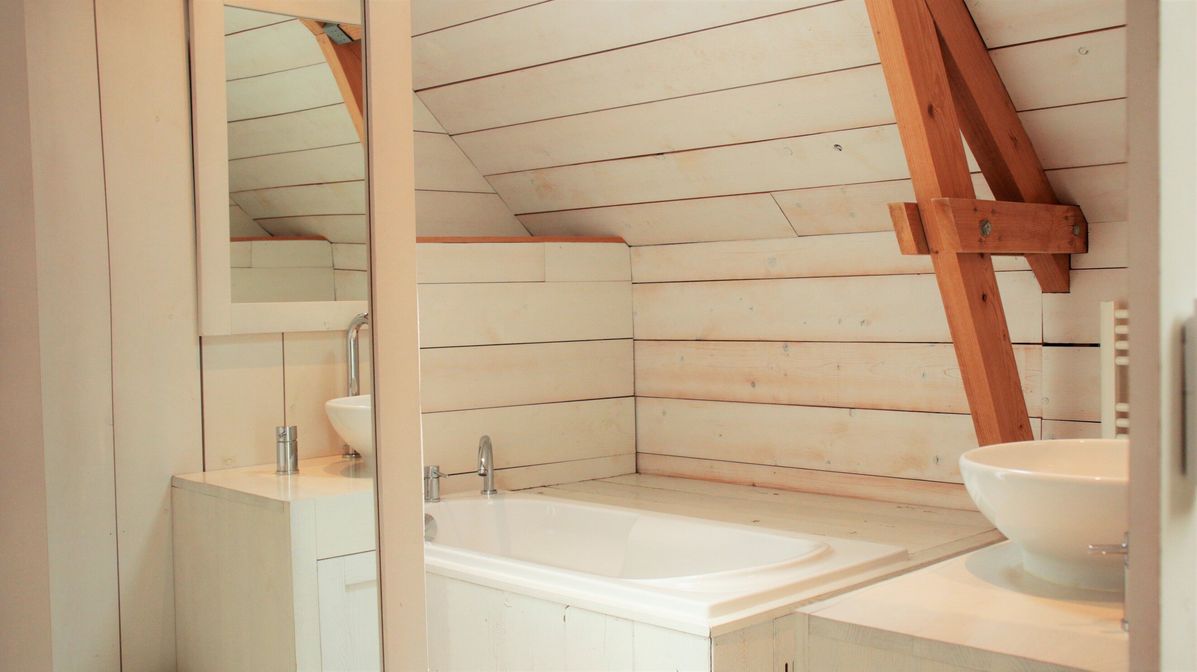 Un baño con pared de listones de madera, lavamanos blanco, espejo y bañera.