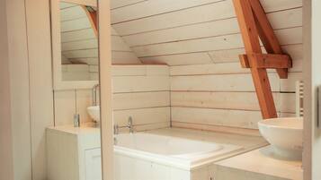 Un baño con pared de listones de madera, lavamanos blanco, espejo y bañera.