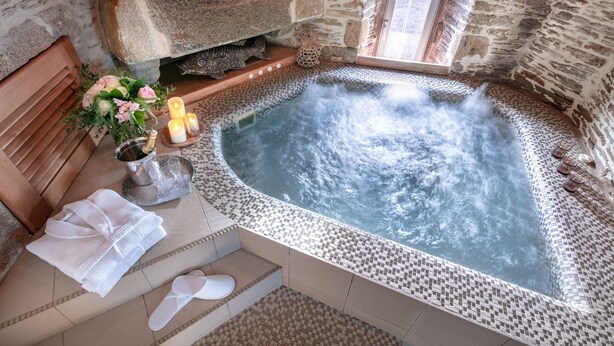 A stone-walled spa area with a hot tub, towels, slippers, and a bouquet of flowers. - La Vinotière (Le Conquet)