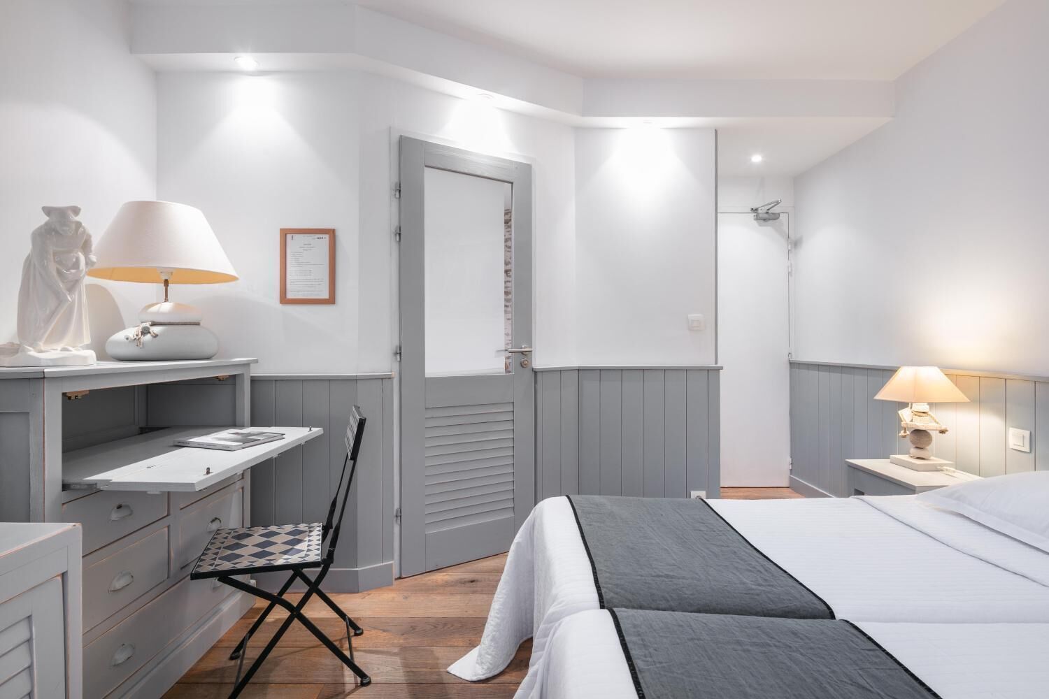 A bedroom with a bed, a desk with a lamp, a chair, and a wardrobe.