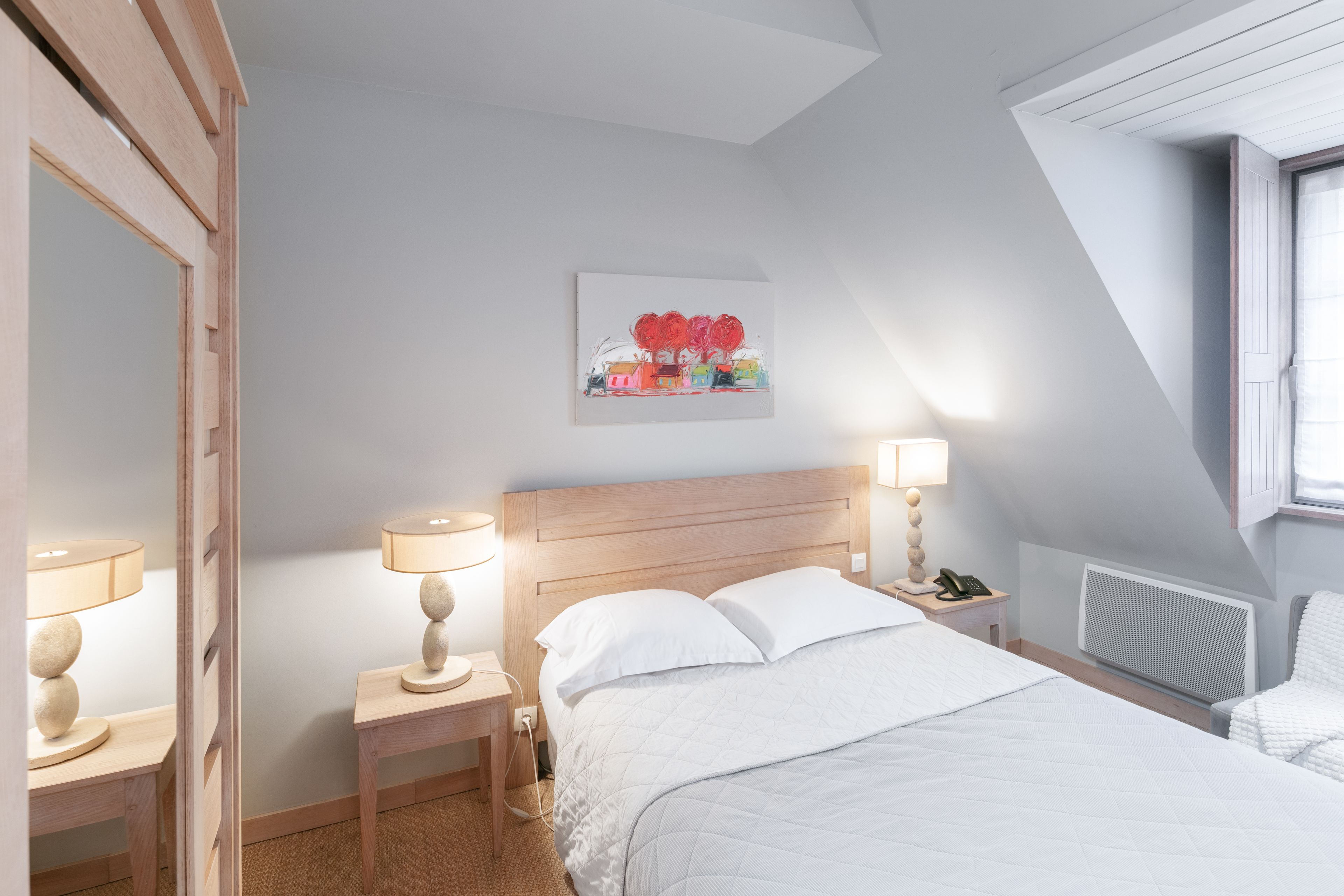 Un dormitorio ordenado con tablero de madera, mesita de noche con lámpara, teléfono en la mesita y un cuadro enmarcado en la pared.